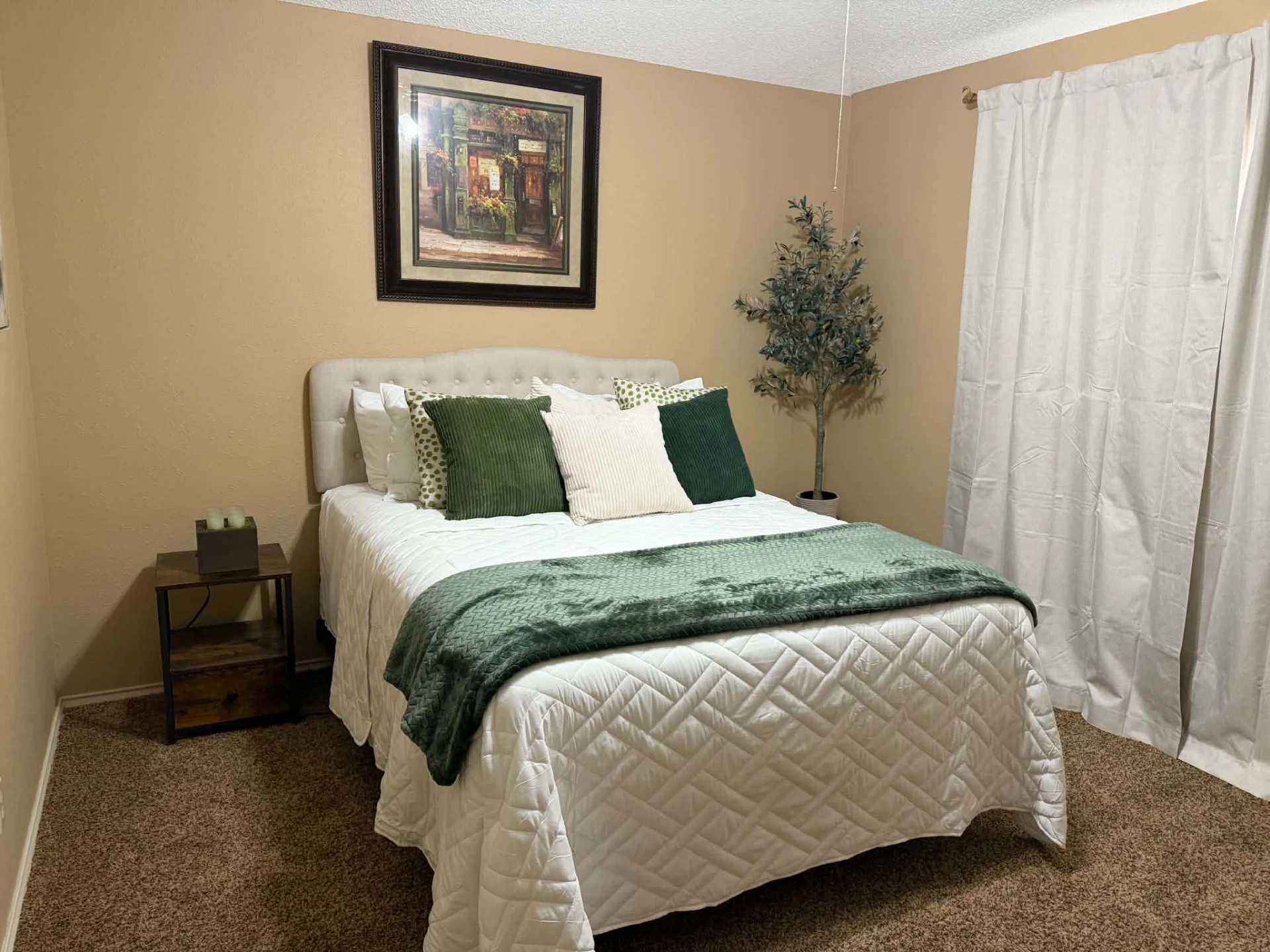 Bedroom 2 with queen bed, tufted headboard, green throw and blackout curtains