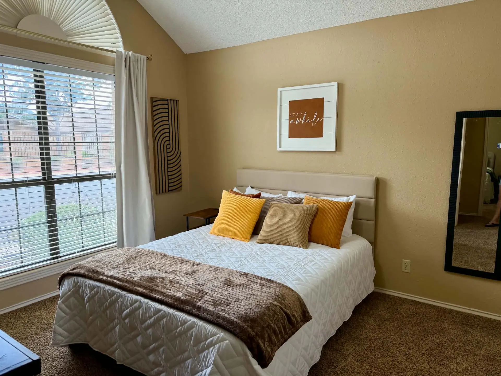 Bedroom 3 with a queen bed, tufted headboard and a 'Stay Awhile' wall sign