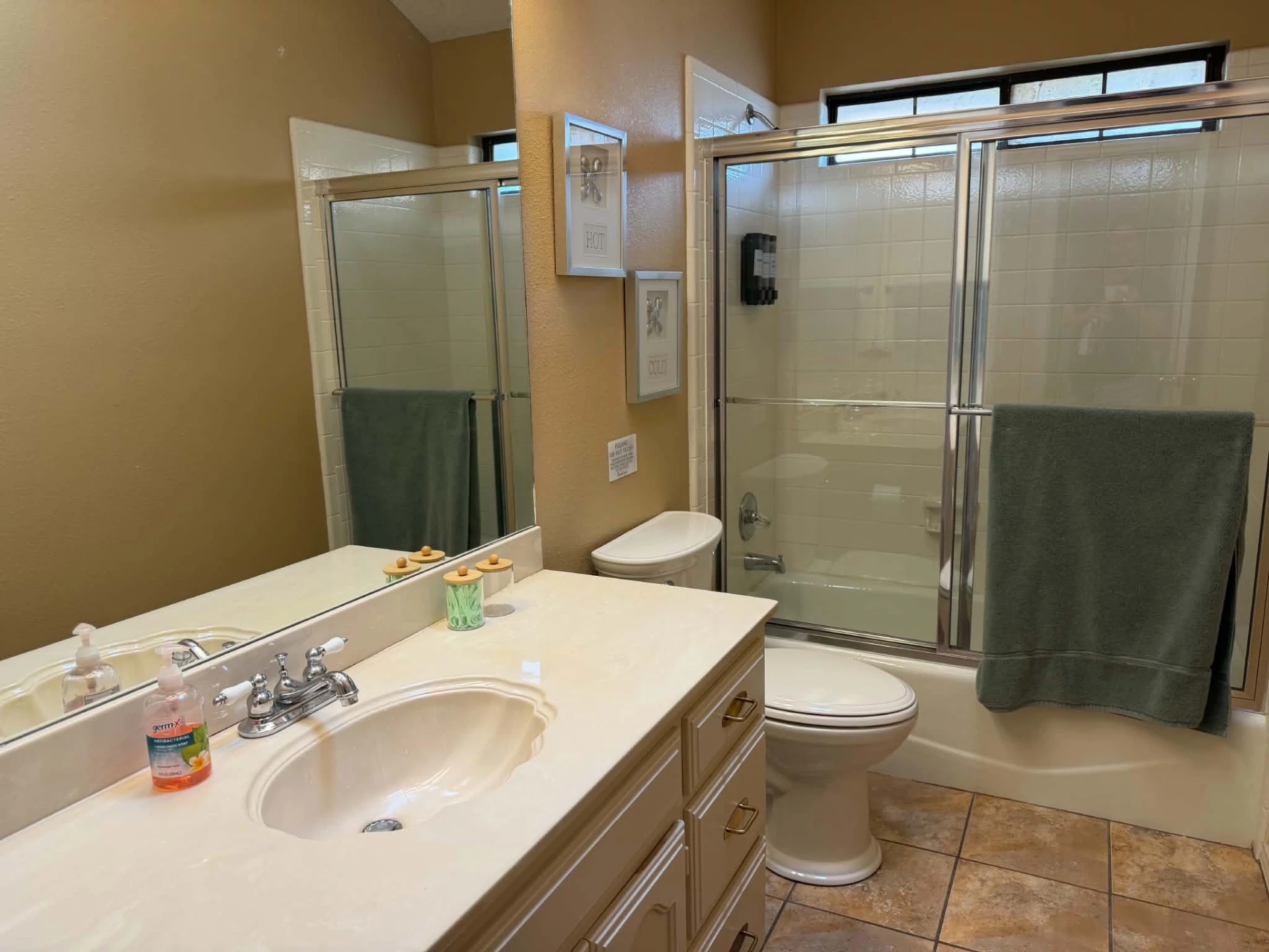 Guest bathroom — vanity, toilet and tub with a sliding glass shower door and a high window