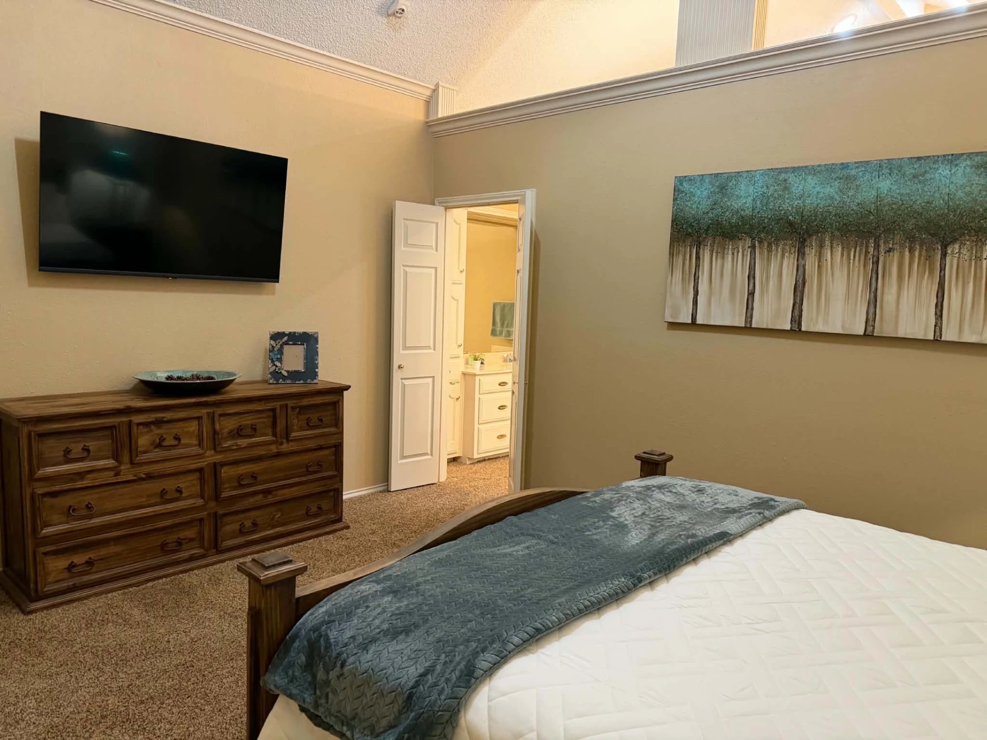 Primary bedroom — 55" wall-mounted smart TV above the dresser, with ensuite bathroom